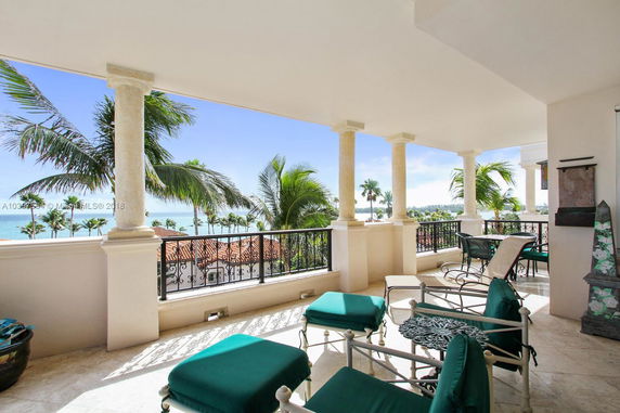 Outdoor seating area with a view of the ocean and palm trees from a balcony.