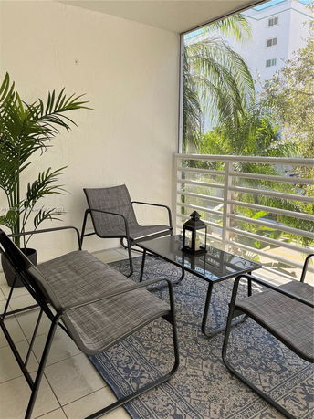 Outdoor seating area on a balcony with a view of trees and a nearby building.