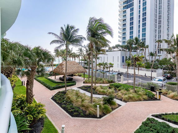 View of surrounding area with a pool, palm trees, and a multi-story building.