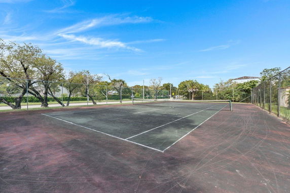Tennis court surrounded by a chain-link fence and trees.