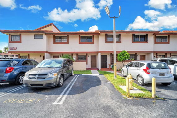 Parking area in front of a townhouse building with multiple parked cars.