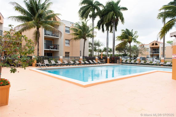 Outdoor swimming pool area with surrounding buildings and palm trees.