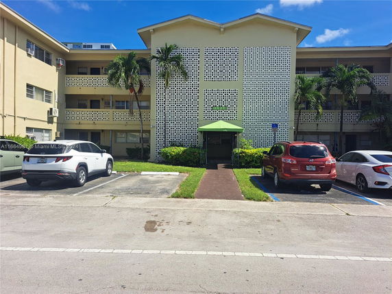 Front view of a three-story residential building with a parking area and lattice design facade.