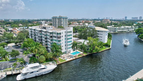 Aerial view of residential buildings near a canal with boats, surrounded by greenery and urban landscape.