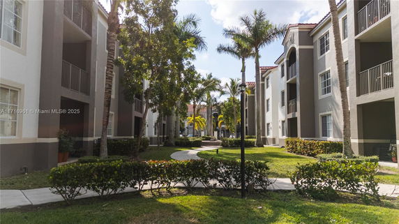 Front view of a multi-story apartment building with balconies and surrounding greenery.