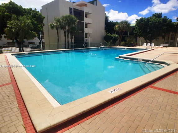 Outdoor swimming pool with a building in the background and poolside seating area.