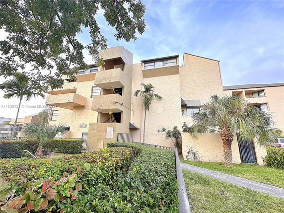 Front view of a multi-story residential building with balconies and palm trees in the foreground.