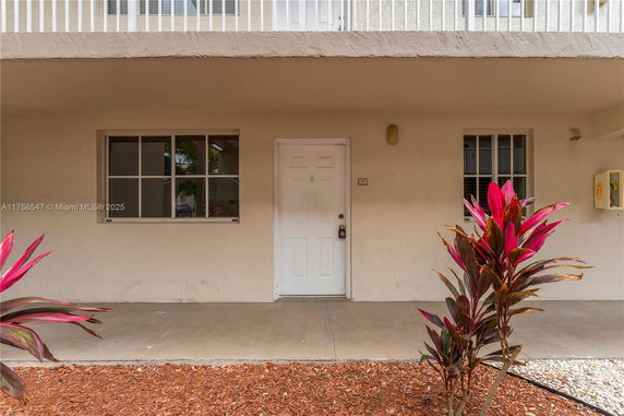 Front view of a house with a white door and two windows, featuring a small porch area.