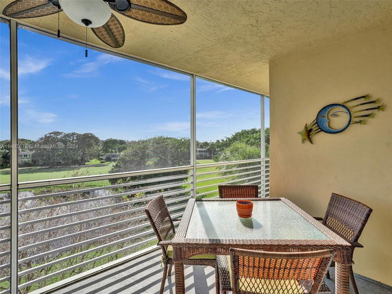 Outdoor balcony with a table and chairs, overlooking a green landscape with trees and distant houses.