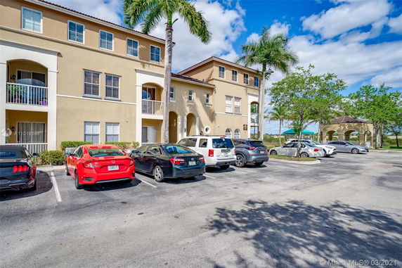 Parking area in front of a multi-story residential building with several parked cars.