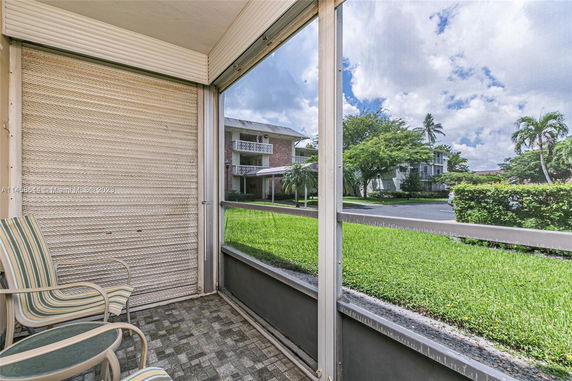 View from a screened patio with outdoor chairs, overlooking green grass and surrounding residential buildings.