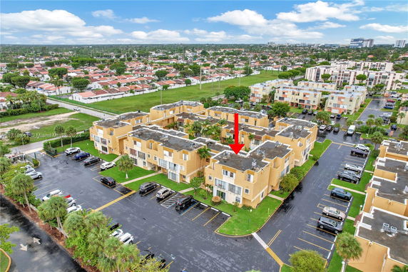 Aerial view of an apartment complex with a parking area and surrounding residential neighborhood.