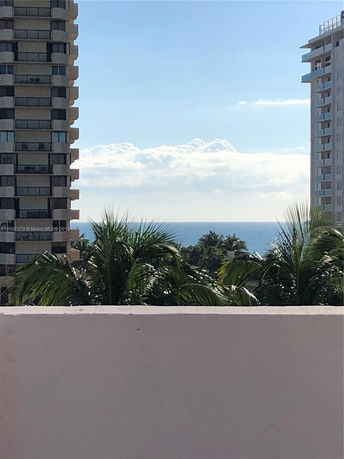 View from a building showing the sea and surrounding palm trees with neighboring high-rise buildings.