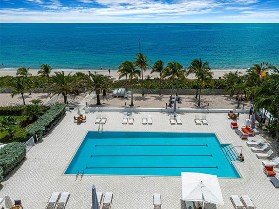 Outdoor swimming pool with lounge chairs near a beach.