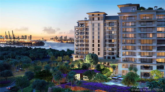 Exterior view of a multi-story apartment building at dusk with city and waterfront in the background.
