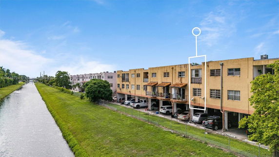 View of building and adjacent canal, showing multiple floors and parking area.