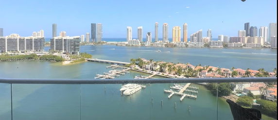 Panoramic view of waterfront buildings and yachts seen from a balcony.