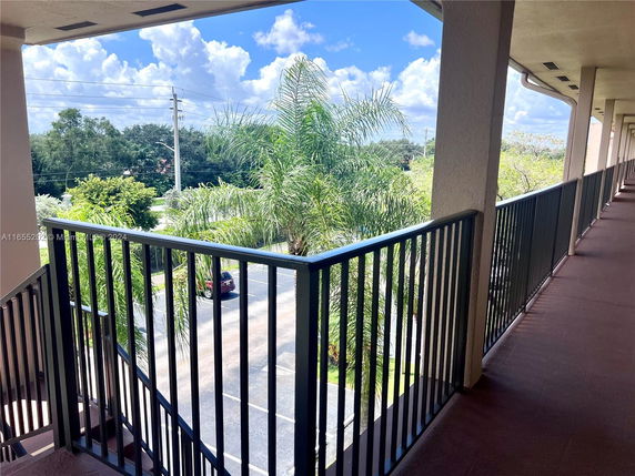 Outdoor view from a building corridor showing trees and a parking area.