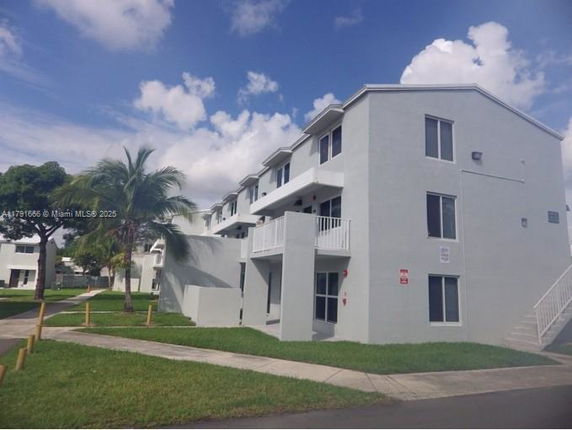 Front view of a multi-story residential building with balconies and exterior stairs.
