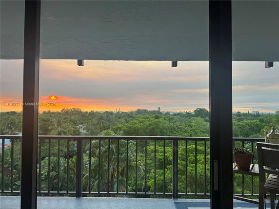 View from a balcony overlooking a lush green area with a distant cityscape at sunset.