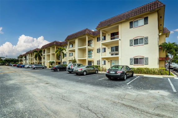View of a multi-story residential building with a parking area in front.