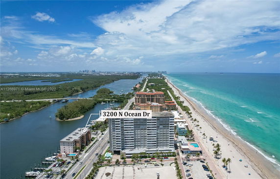 Aerial view of a coastal area showing a beach, ocean, and a row of buildings, including one labeled with an address.