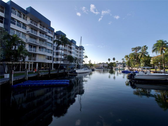 View of a waterfront building with multiple floors and balconies, next to a canal with boats docked.