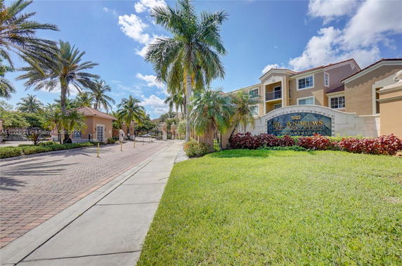 Front view of a condominium building with palm trees and a sign.