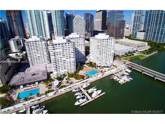 Aerial view of multiple high-rise buildings near a waterfront with boats docked at a marina.