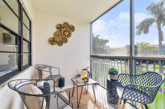 Balcony with decorative wall art, chairs, and table overlooking a landscaped area.