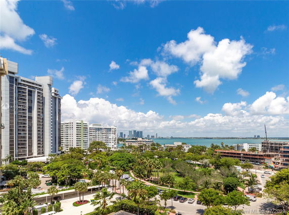 View of several tall buildings with a clear sky and ocean in the background.