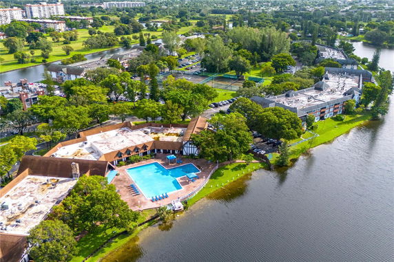 Aerial view of a building complex with a swimming pool, surrounded by trees and a lake.