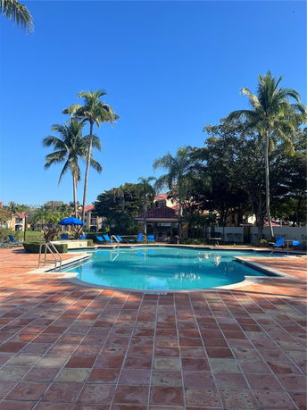 Outdoor swimming pool with sun loungers and palm trees.