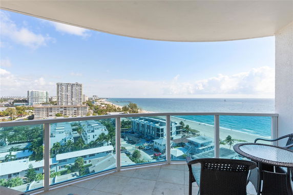 View from a balcony overlooking the ocean and beachfront buildings.