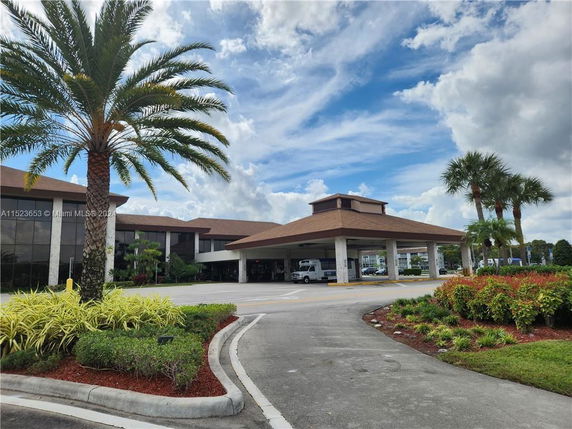 Front view of a large building with a covered entrance and palm trees.