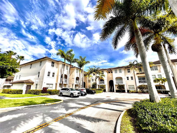 Front view of a multi-story residential building with balconies and palm trees.