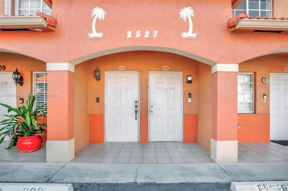 Front view of a building entrance with two white doors and decorative palm tree elements.
