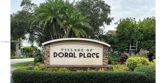 Entrance sign for Village of Doral Place surrounded by greenery.