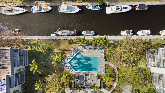 Aerial view of a swimming pool surrounded by trees near a waterway with boats docked.