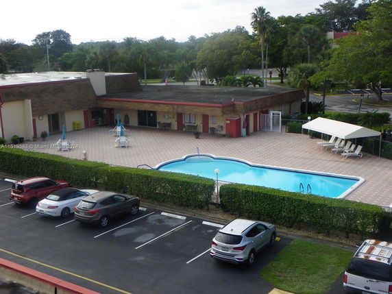 Outdoor swimming pool area with adjacent building and parking spaces.