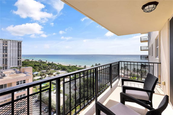 Balcony with chairs overlooking ocean and buildings.