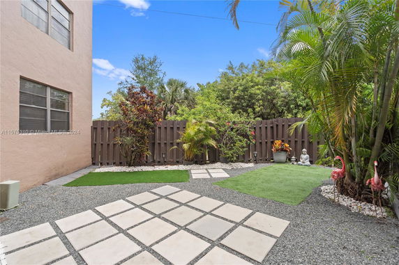 Outdoor view of a fenced garden area with paving stones and greenery near a building.