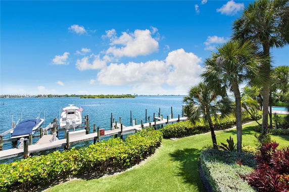 View of a waterfront area with boats docked along a wooden pier and lush greenery.