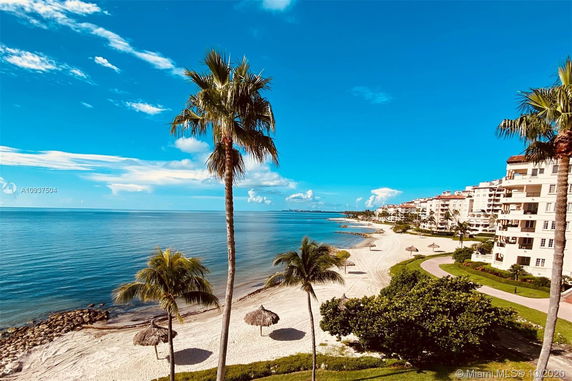Beachfront view with a large building and palm trees along a sandy shore.