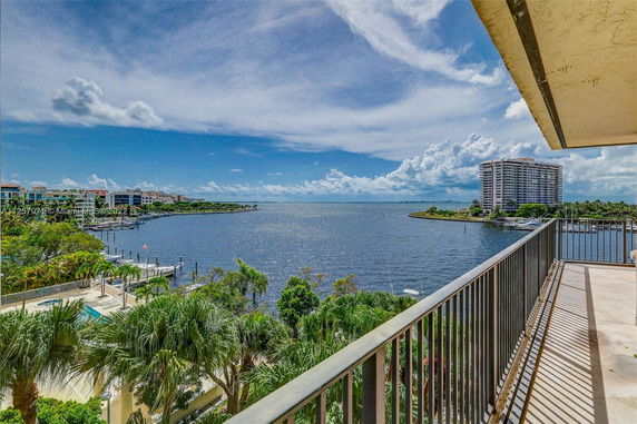Panoramic view from a balcony overlooking a body of water with distant buildings and a clear blue sky.