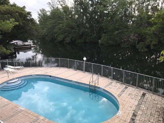 Outdoor swimming pool with brick paving and railings by a waterway.