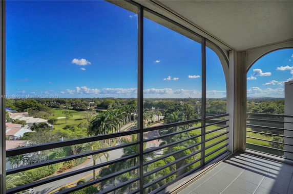 Panoramic view from a building's balcony, showing a landscape with trees and a clear blue sky.