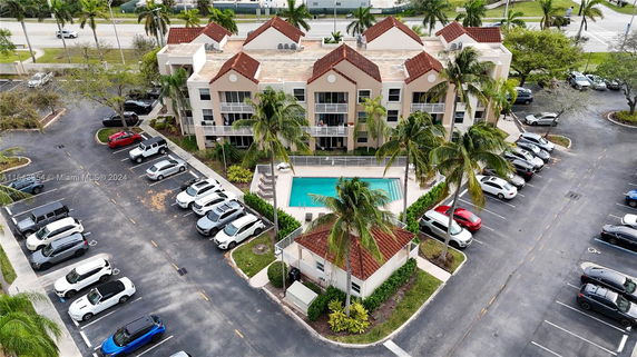 Aerial view of an apartment complex with a swimming pool in the center and a parking area surrounding it.