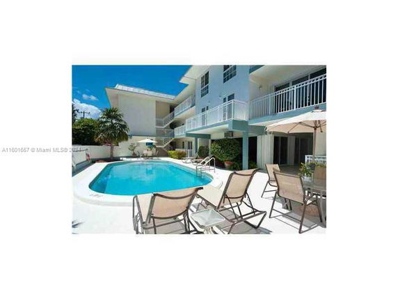 Outdoor swimming pool area with lounge chairs and a multi-story building.