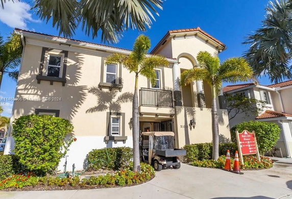 Front view of a two-story house with a balcony and palm trees.